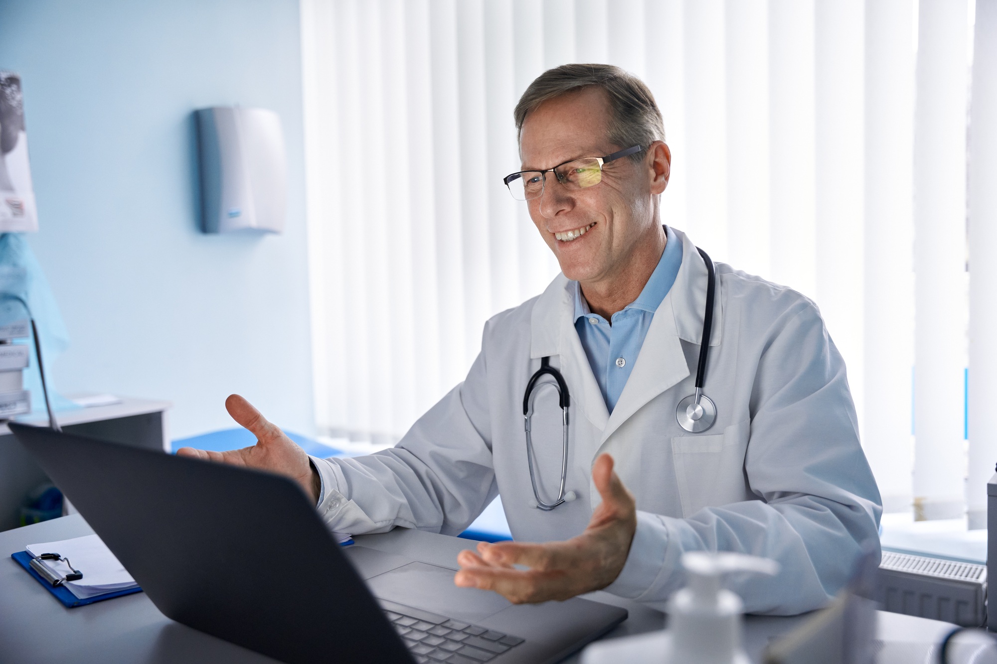 Happy old male doctor consulting patient online by video call on laptop.